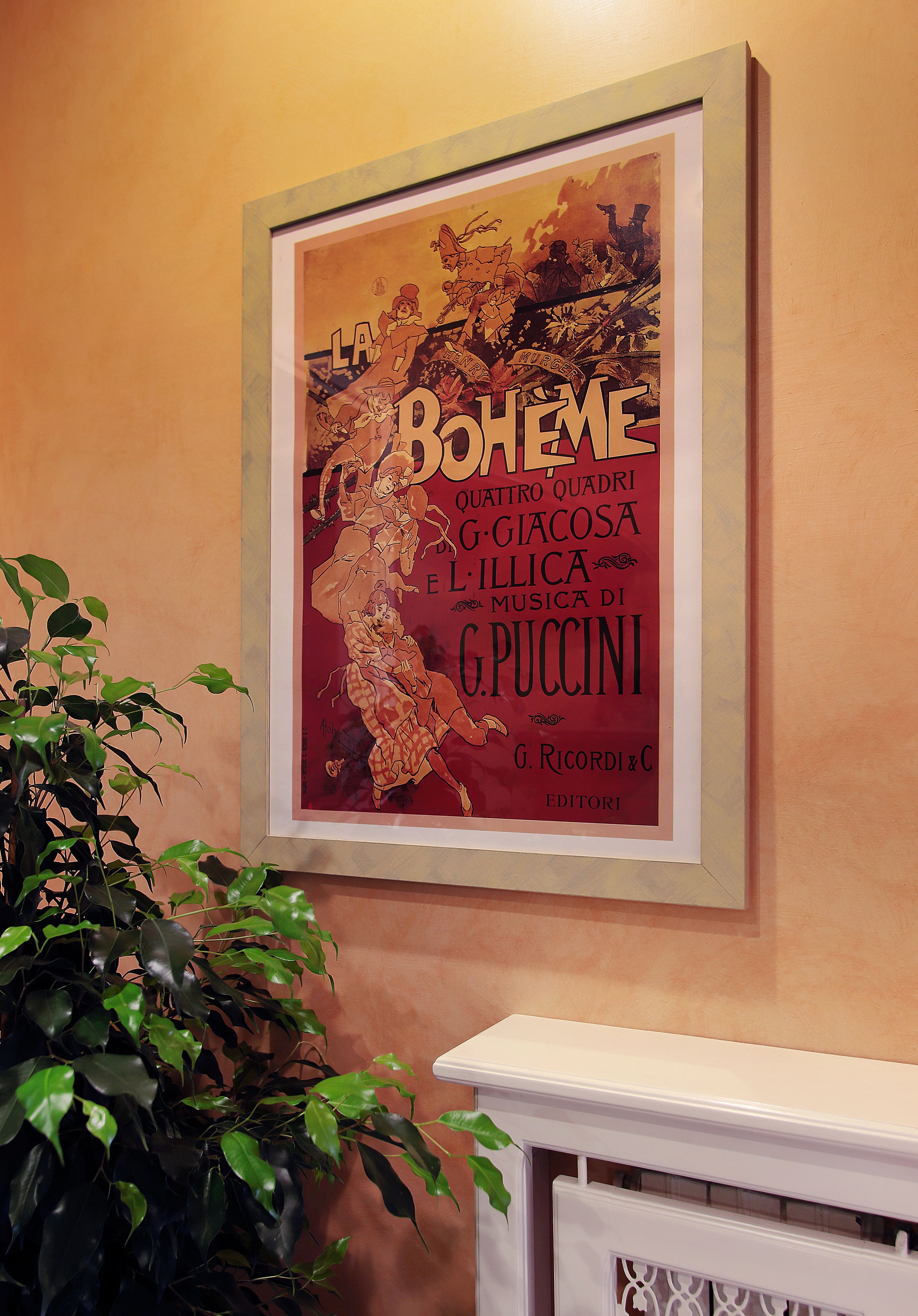 A framed poster on a wall with a plant in the foreground.