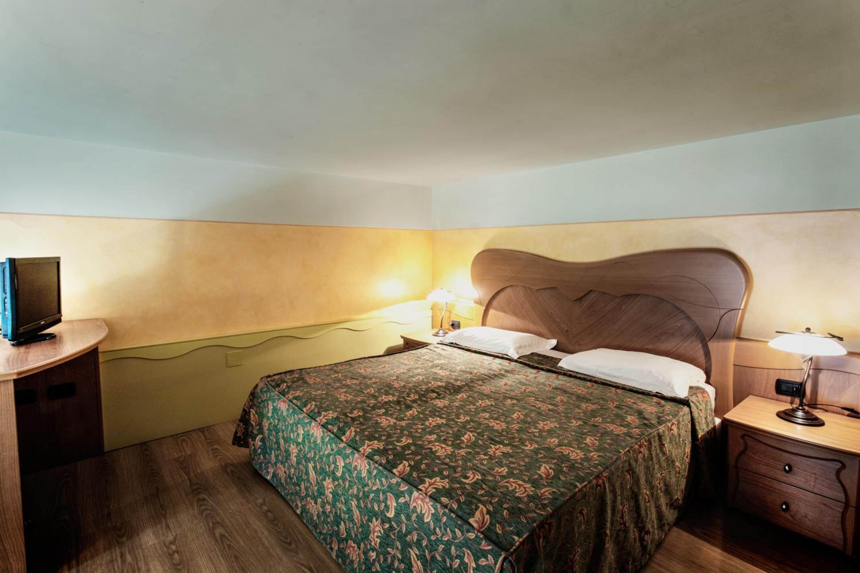 Une chambre à coucher avec un lit, des tables de chevet, une lampe et un téléviseur posé sur un meuble.