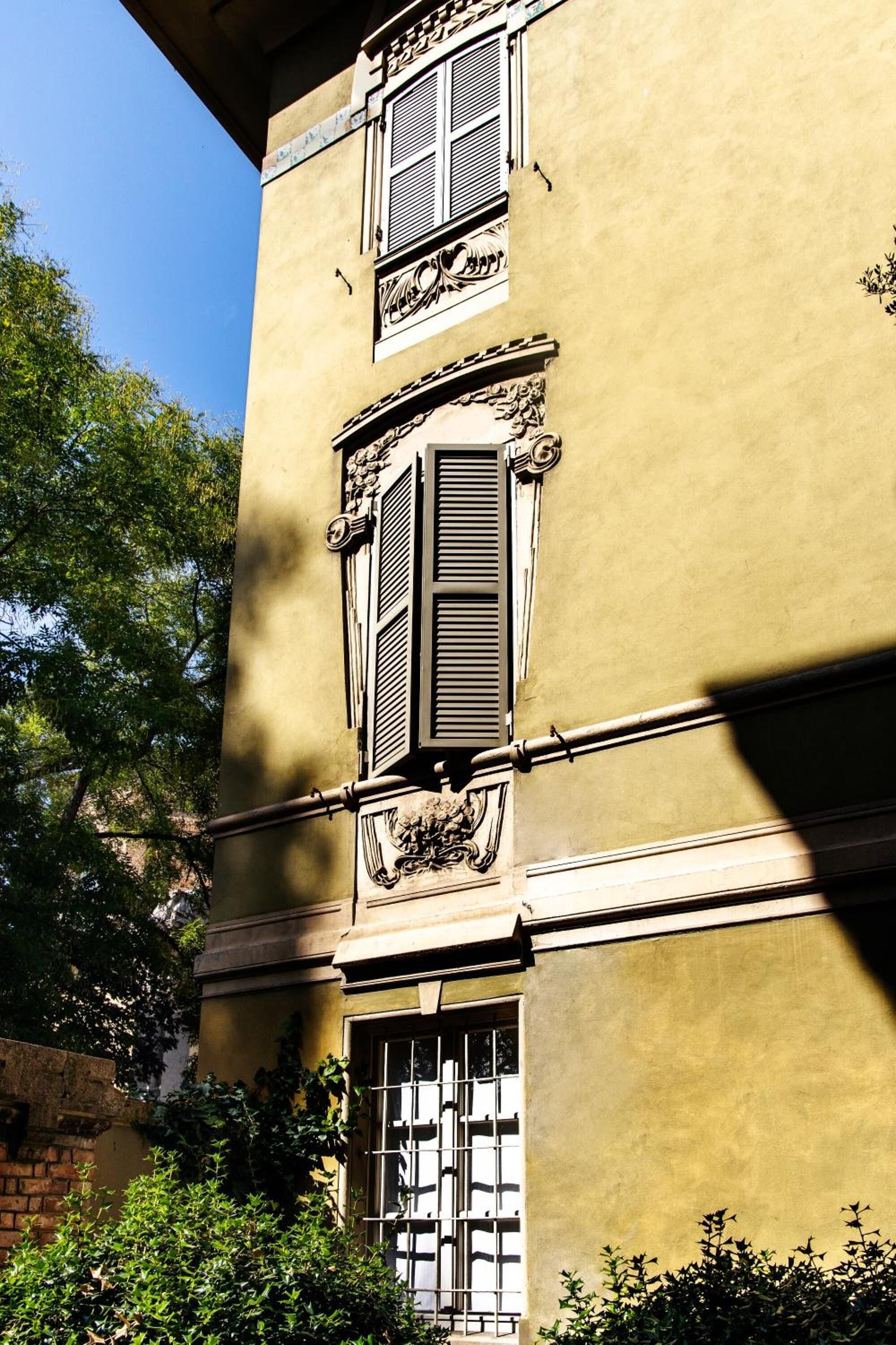 A building with a yellow facade, ornate window shutters, and decorative moldings.
