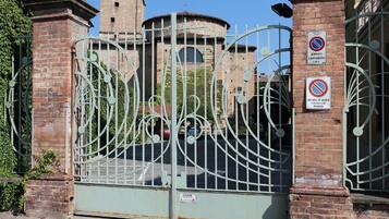 A gated entrance with a metal gate, brick walls, and a tower in the background.