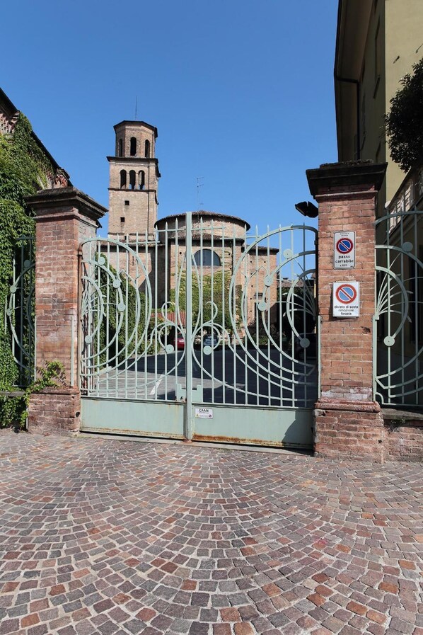 A gated entrance with a metal gate, brick walls, and a tower in the background.