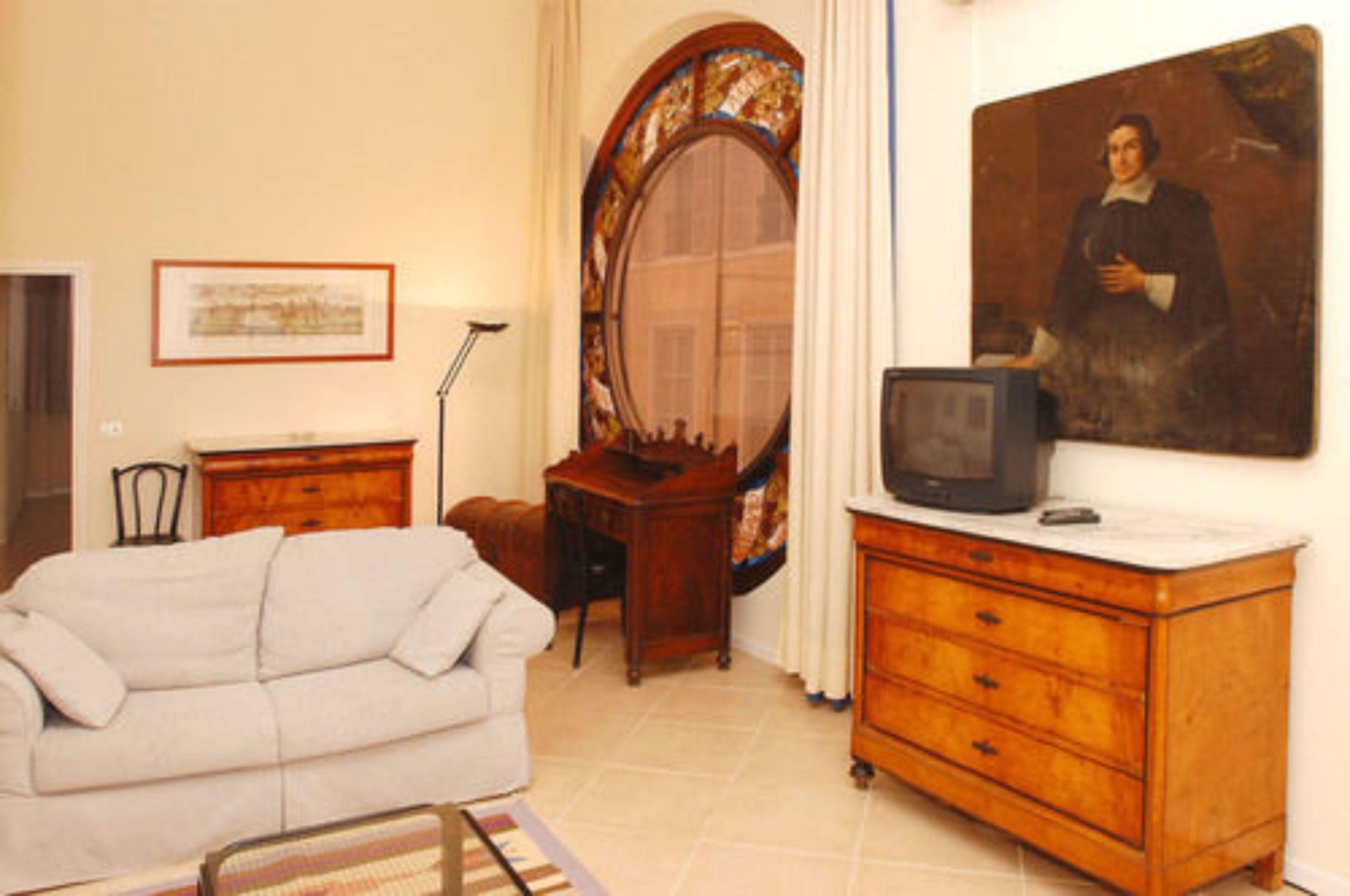 A room with a white sofa, a wooden dresser, a mirror, a framed picture, and a television on the dresser.