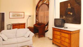 A room with a white sofa, a wooden dresser, a mirror, a framed picture, and a television on the dresser.