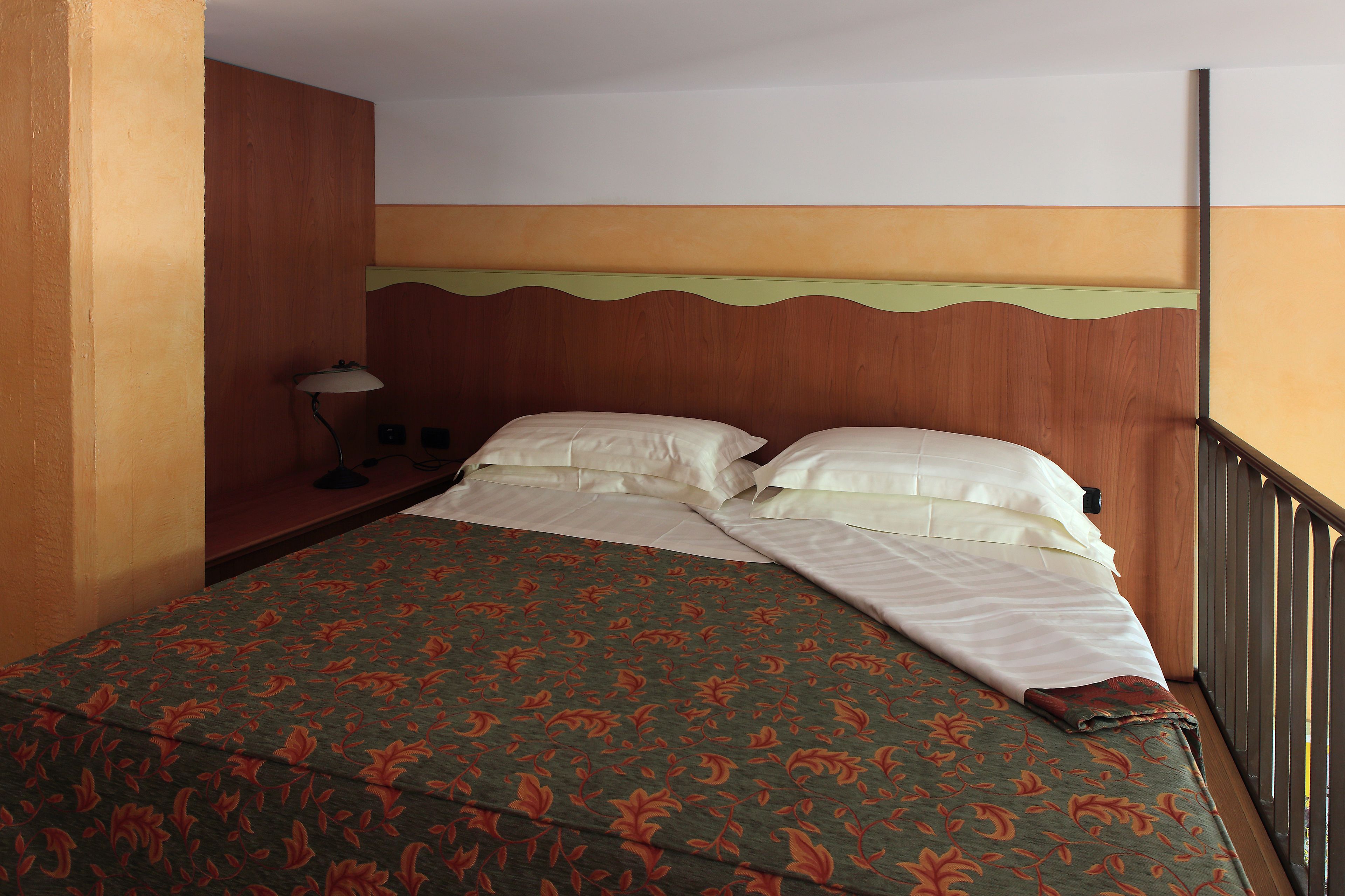 Una cama bien hecha con una colcha estampada con motivos florales, una lámpara de noche y un cabecero de madera.