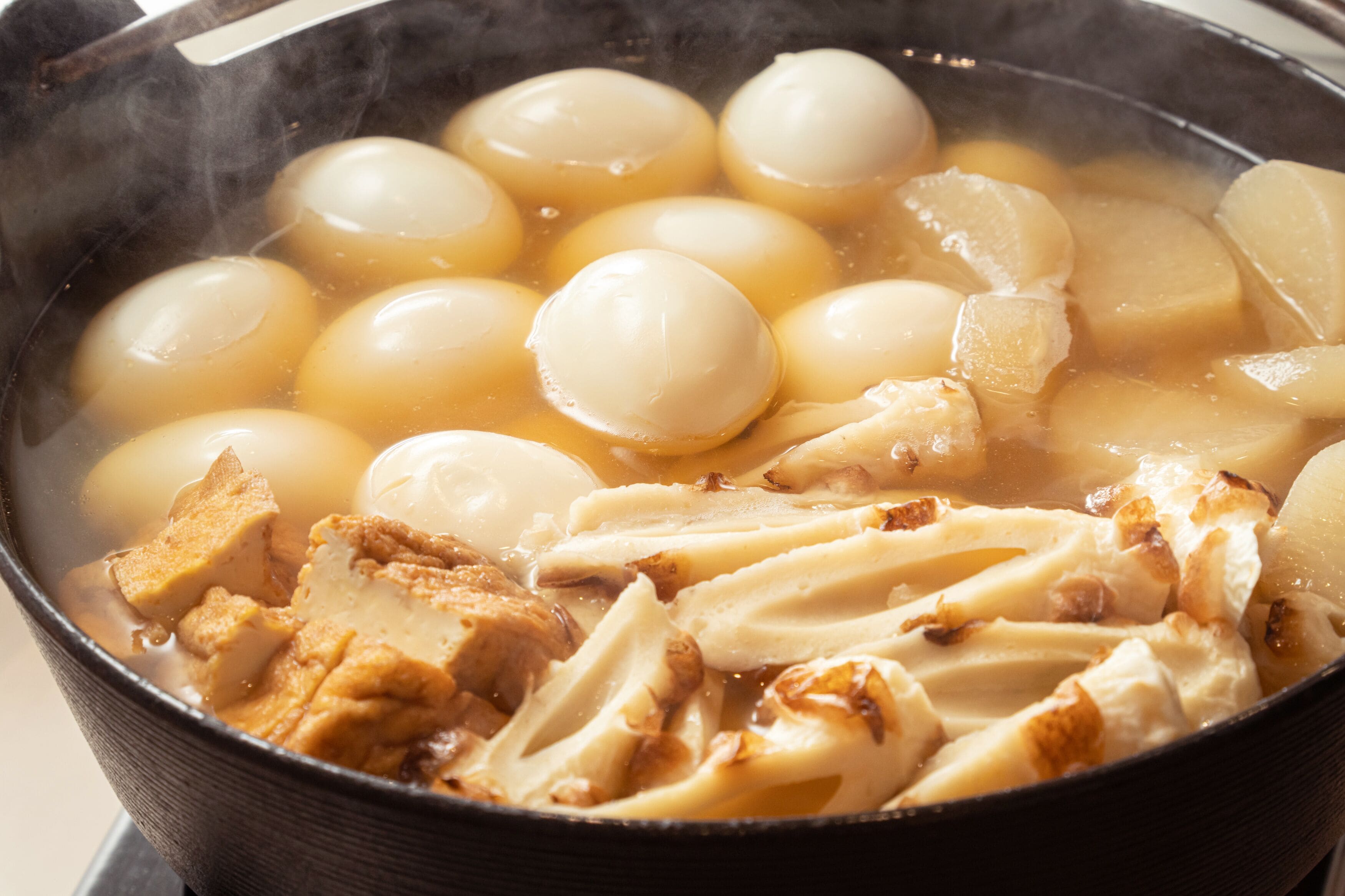 A pot of soup with round, boiled eggs and pieces of meat.