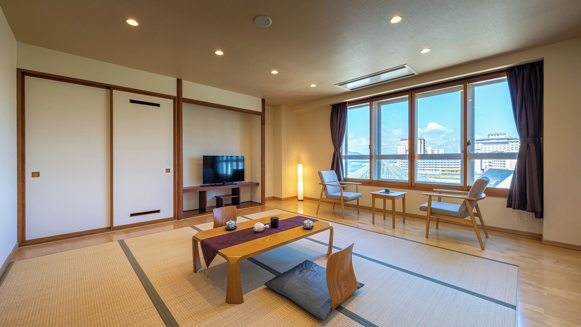 A modern living room with tatami mats, a TV, a sofa, and a view of the city.