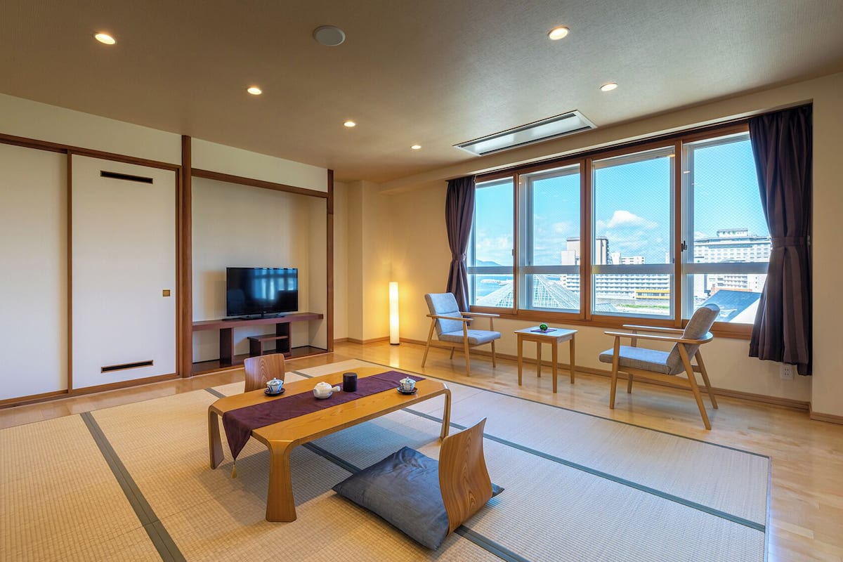 A modern living room with tatami mats, a TV, a sofa, and a view of the city.