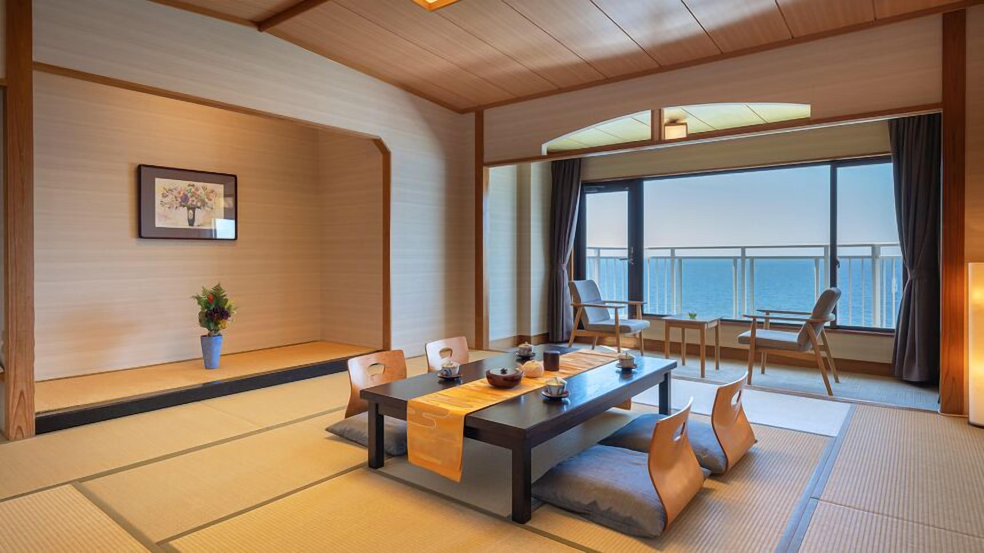 A traditional Japanese-style room with tatami flooring, a low table with cushions, and a view of the sea.