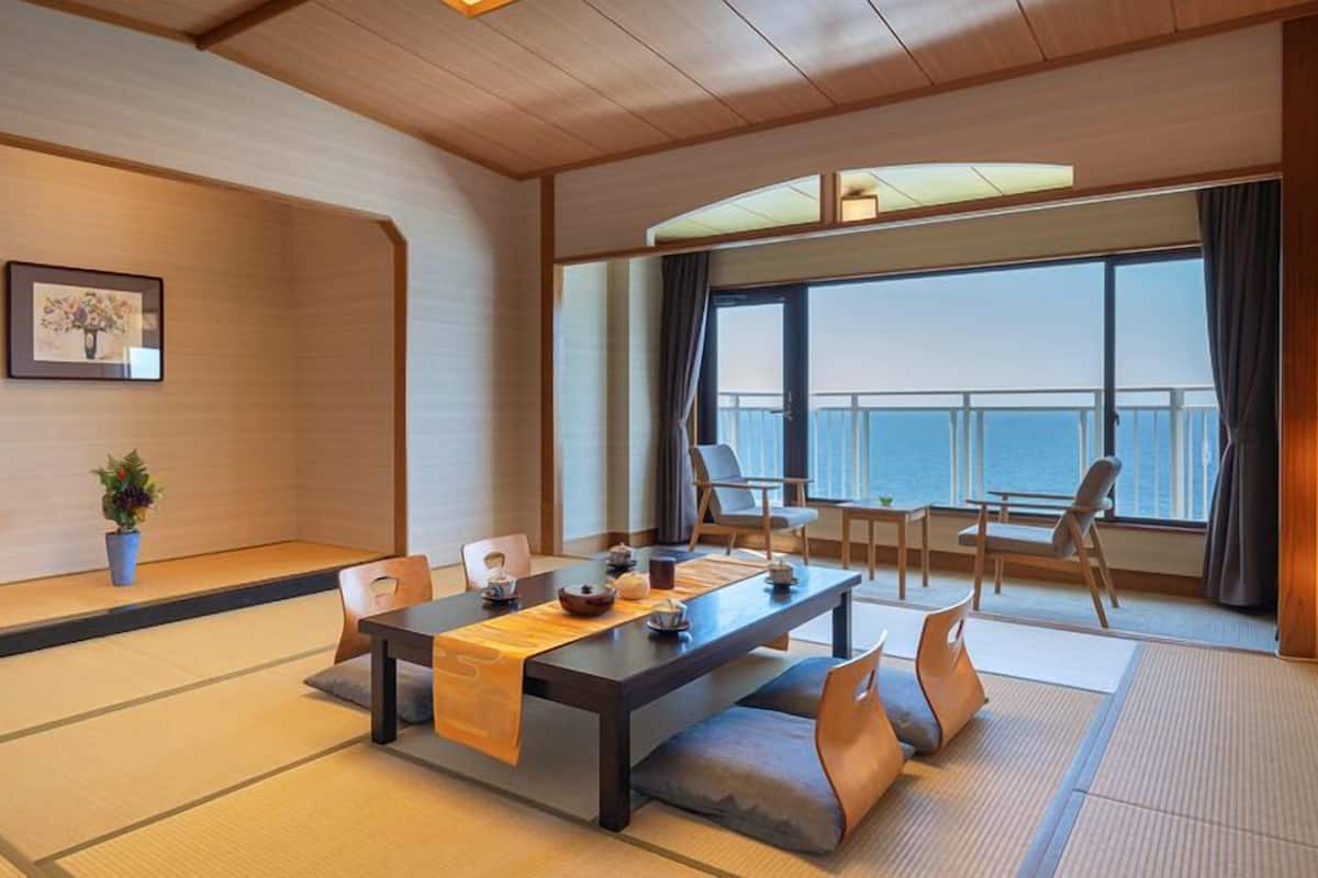 A traditional Japanese-style room with tatami flooring, a low table with cushions, and a view of the sea.