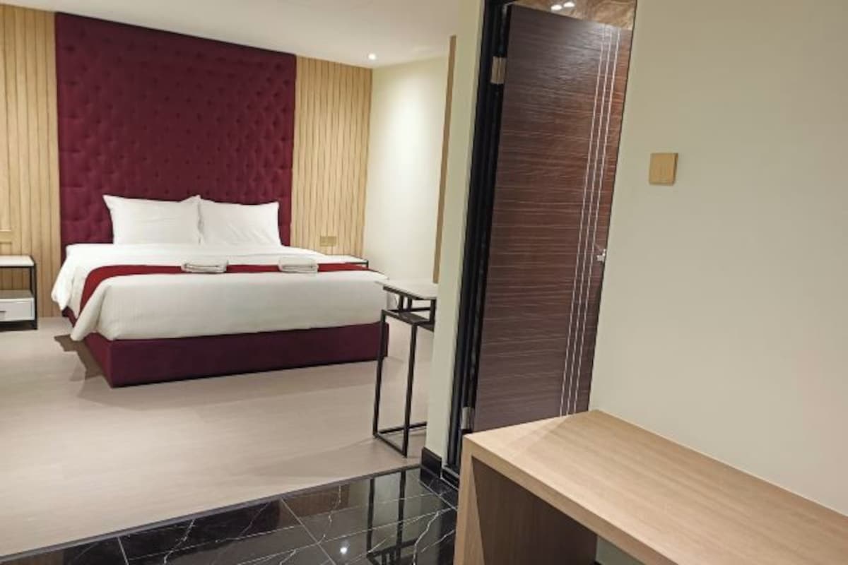 A modern hotel room with a large bed, a wooden nightstand, and a wooden bench.