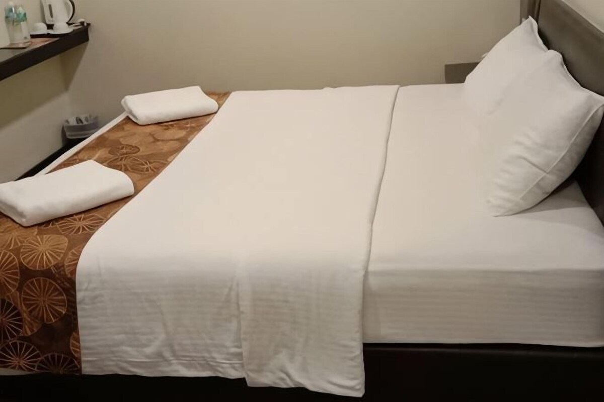 Una cama bien hecha con sábanas blancas, un edredón marrón estampado y un cabecero.