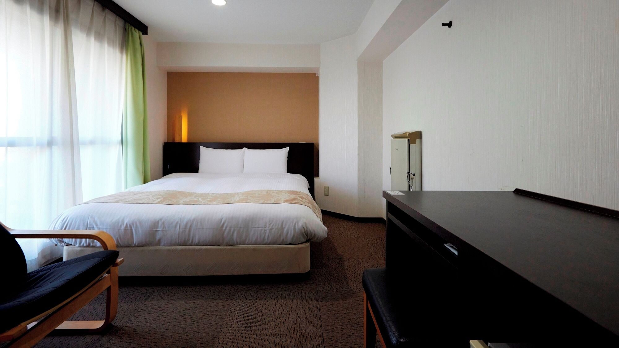 A hotel room with a bed, a desk, a chair, and a wardrobe.