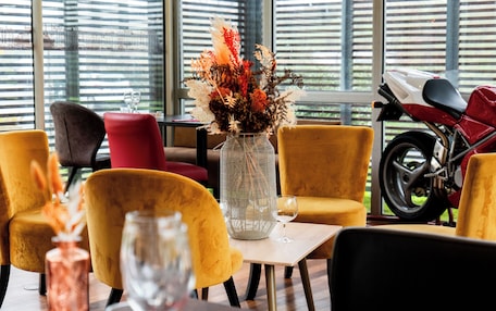 A dining area with yellow chairs, a table with a vase of flowers, and a motorcycle in the background.