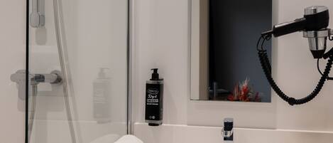 A modern bathroom with a glass-enclosed shower, a white sink, and a hairdryer mounted on the wall.