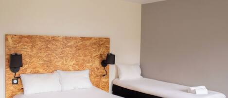 A hotel room with two beds, each with white bedding and pillows, and a wooden headboard.