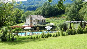 A large house with a swimming pool, surrounded by lush greenery and hills.