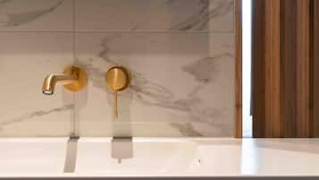Ein Badezimmer mit einem weißen Waschbecken, goldenen Wasserhähnen und Marmorfliesen.