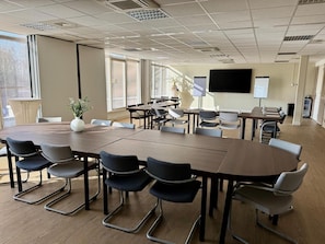 Une salle de confĂ©rence Ă©quipĂ©e dâune grande table, de chaises, dâun Ă©cran de projection et dâun tableau blanc.