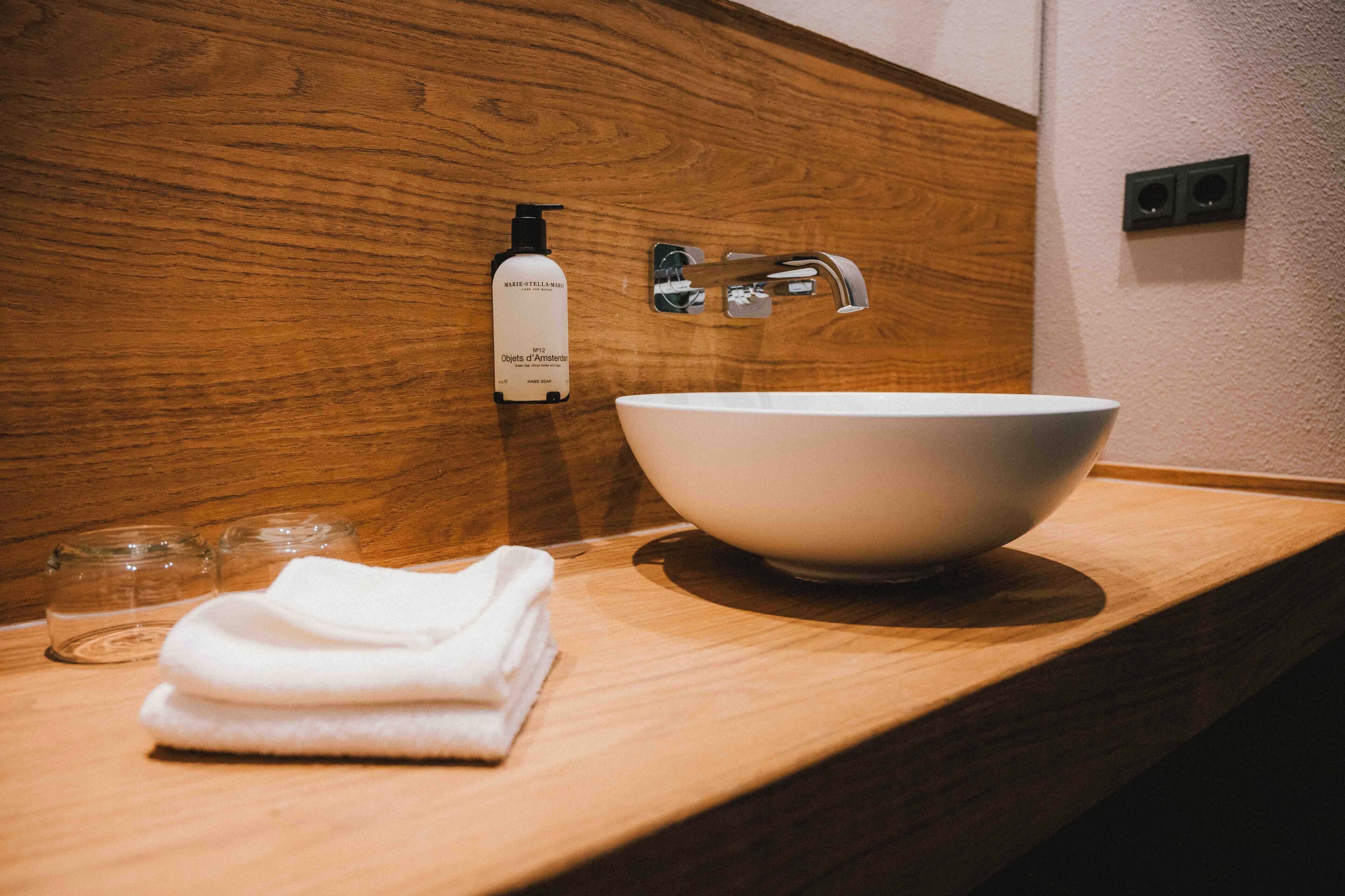 Un baño con tocador de madera, un lavabo blanco, una toalla y una botella de jabón para manos.