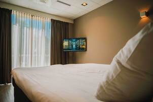 Une chambre d’hôtel avec un grand lit, une fenêtre avec des rideaux et un téléviseur fixé au mur.