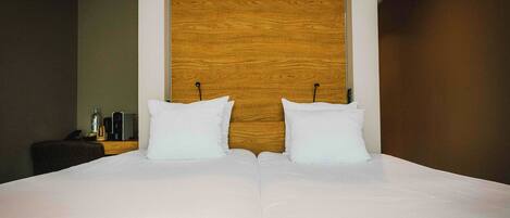 Una cama grande con ropa de cama blanca y dos almohadas, un cabecero de madera y una mesita de noche con una botella y un teléfono.