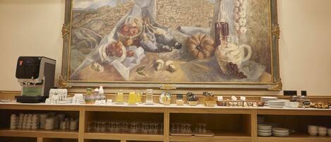 Un comedor con un cuadro grande de bodegón, una cafetera y vajilla ordenada en estantes.