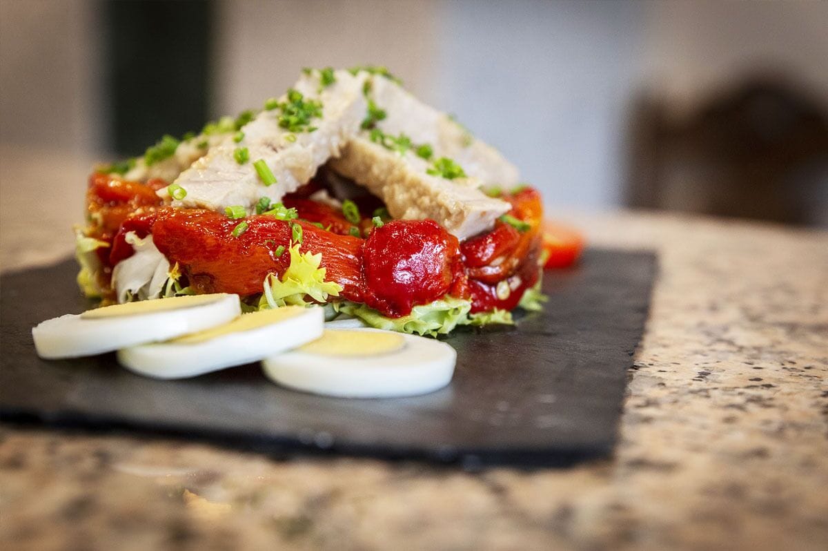 A salad with sliced meat, tomatoes, and boiled eggs on a slate plate.