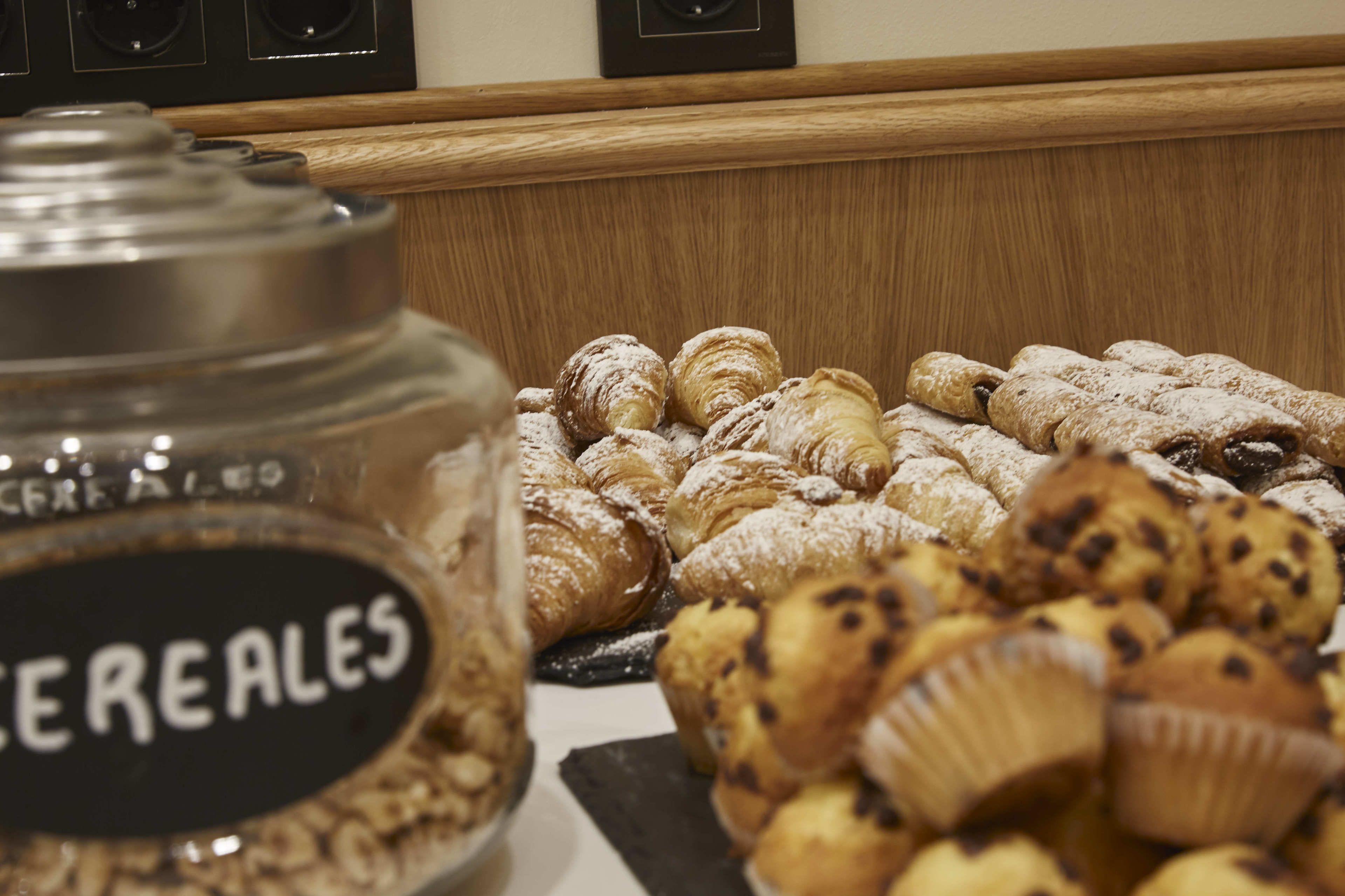 A display of assorted pastries and a jar labeled "CEREALES" in a bakery setting.