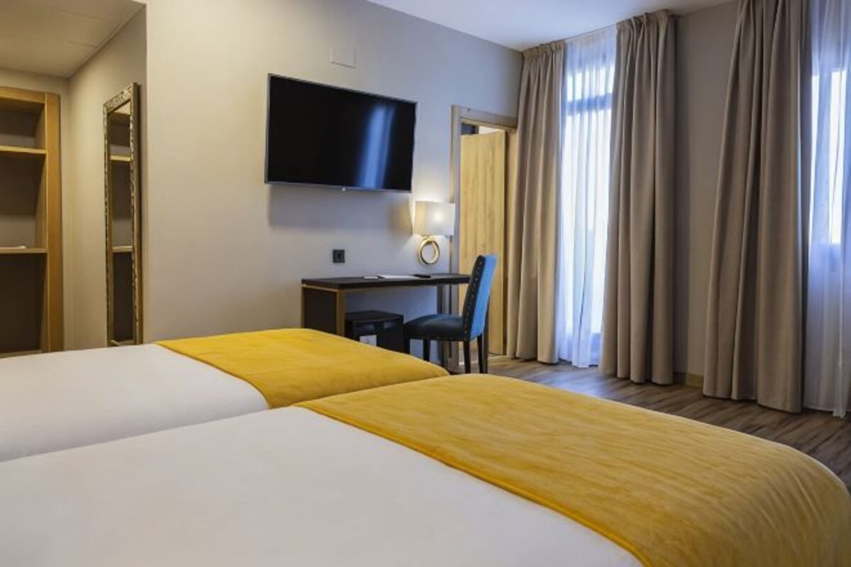A hotel room with two beds, a desk with a chair, a television, and a window with curtains.