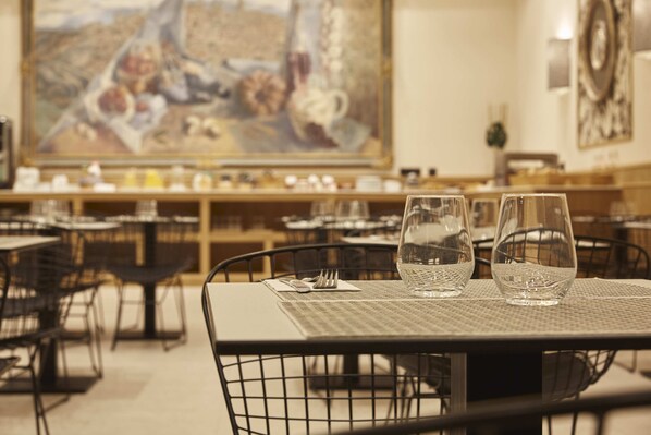 A restaurant interior with tables set for dining, a large painting on the wall, and a bar area in the background. - Hotel Zentral Mayoral (Toledo)