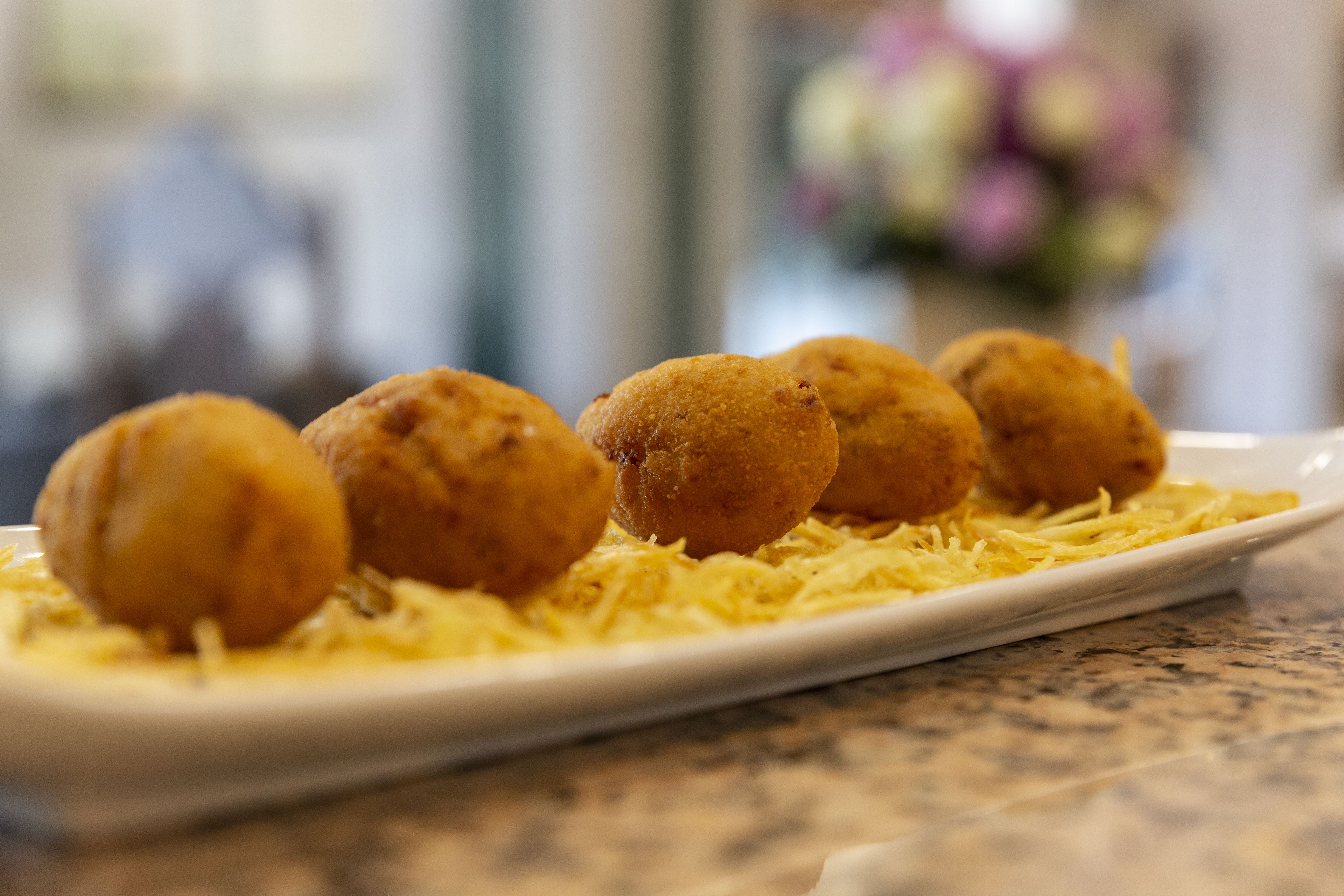 Un plato de porciones redondas y doradas fritas sobre una cama de queso rallado.