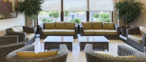 A spacious living area with wicker furniture, large windows, and potted plants.