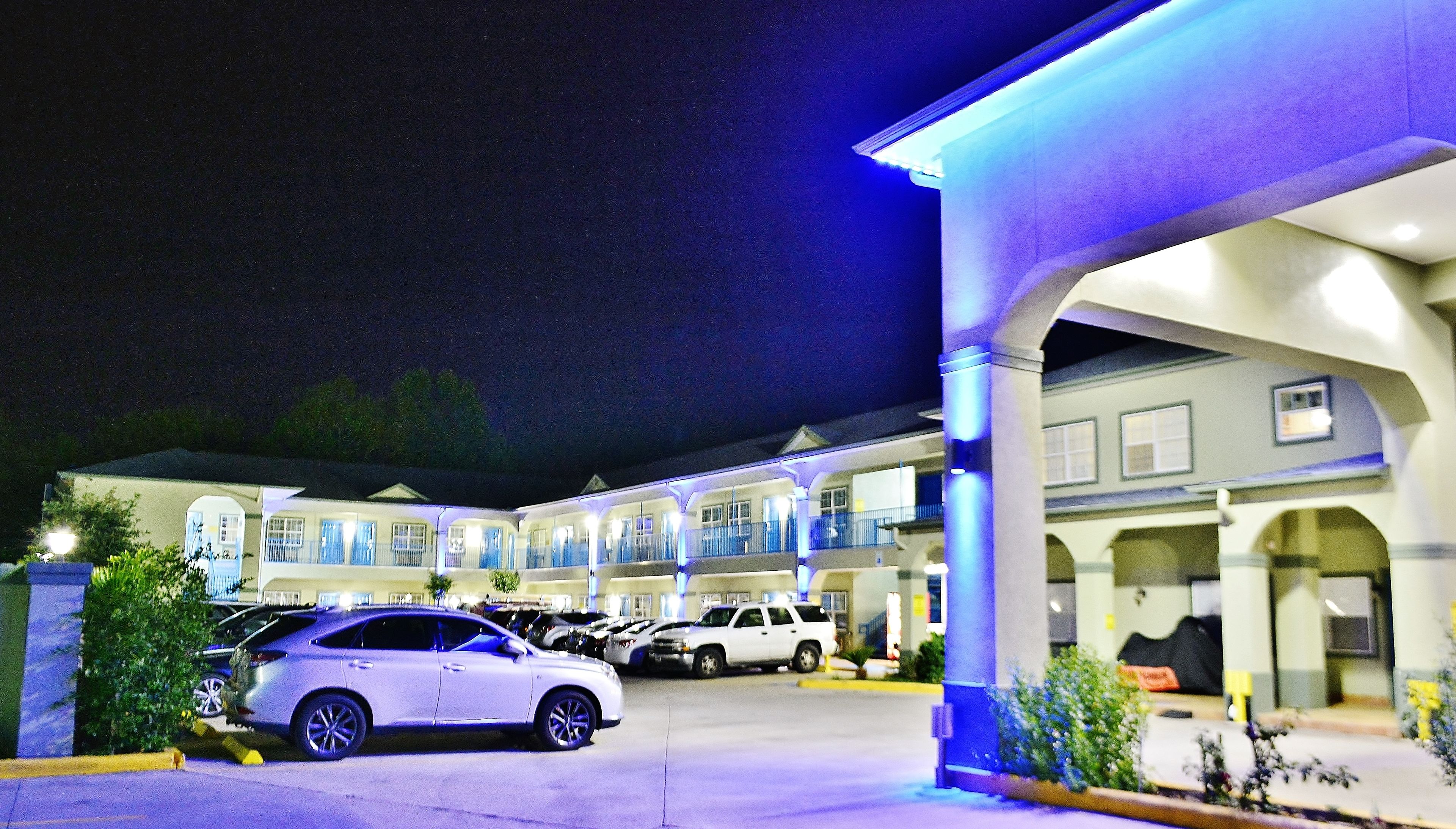 A hotel with multiple balconies, a parking lot, and a covered walkway.