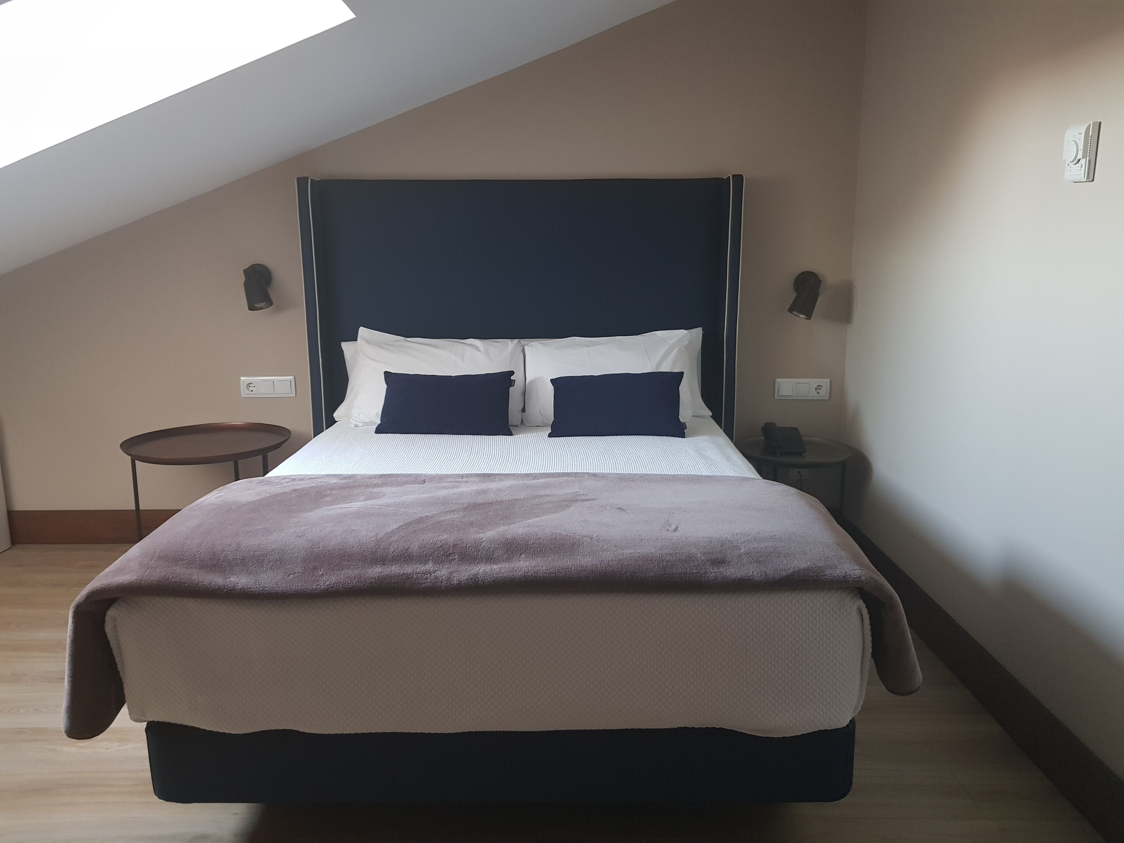 A bedroom with a bed, a small round table, a bedside lamp, and a wall-mounted phone.