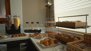 A breakfast buffet with various pastries and bread, including croissants and muffins, displayed on trays and in baskets.