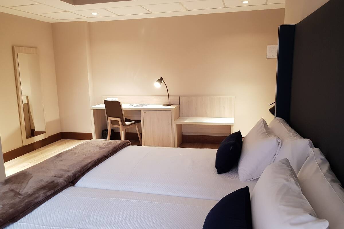 A hotel room with a bed, a desk, a chair, and a mirror.