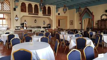 Un salón de banquetes con mesas redondas y sillas azules, una zona de bar y faroles decorativos.