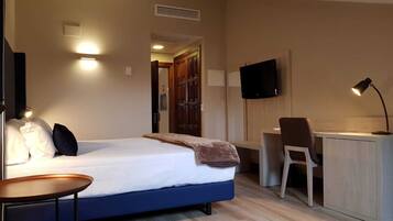 A hotel room with a bed, a desk, a chair, a TV, and a lamp.