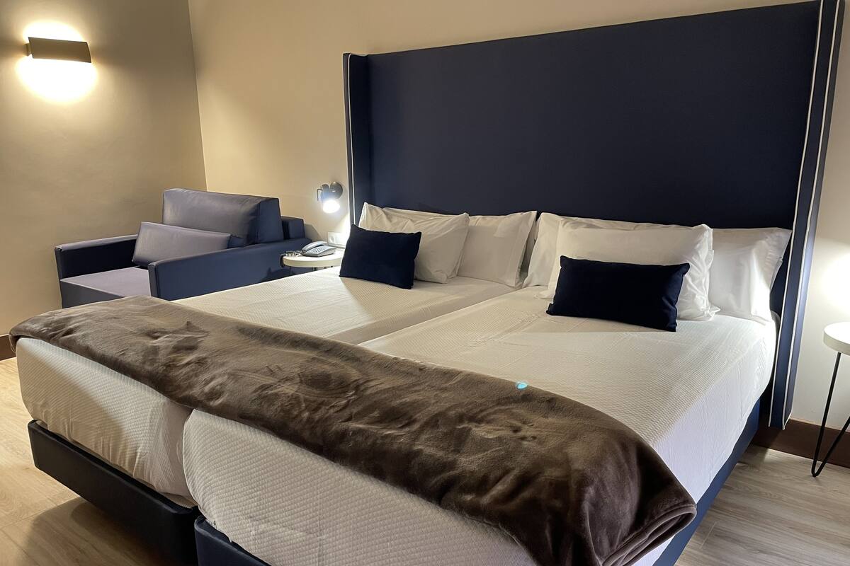 A hotel room with a large bed, two bedside tables, a chair, and a wall-mounted light.