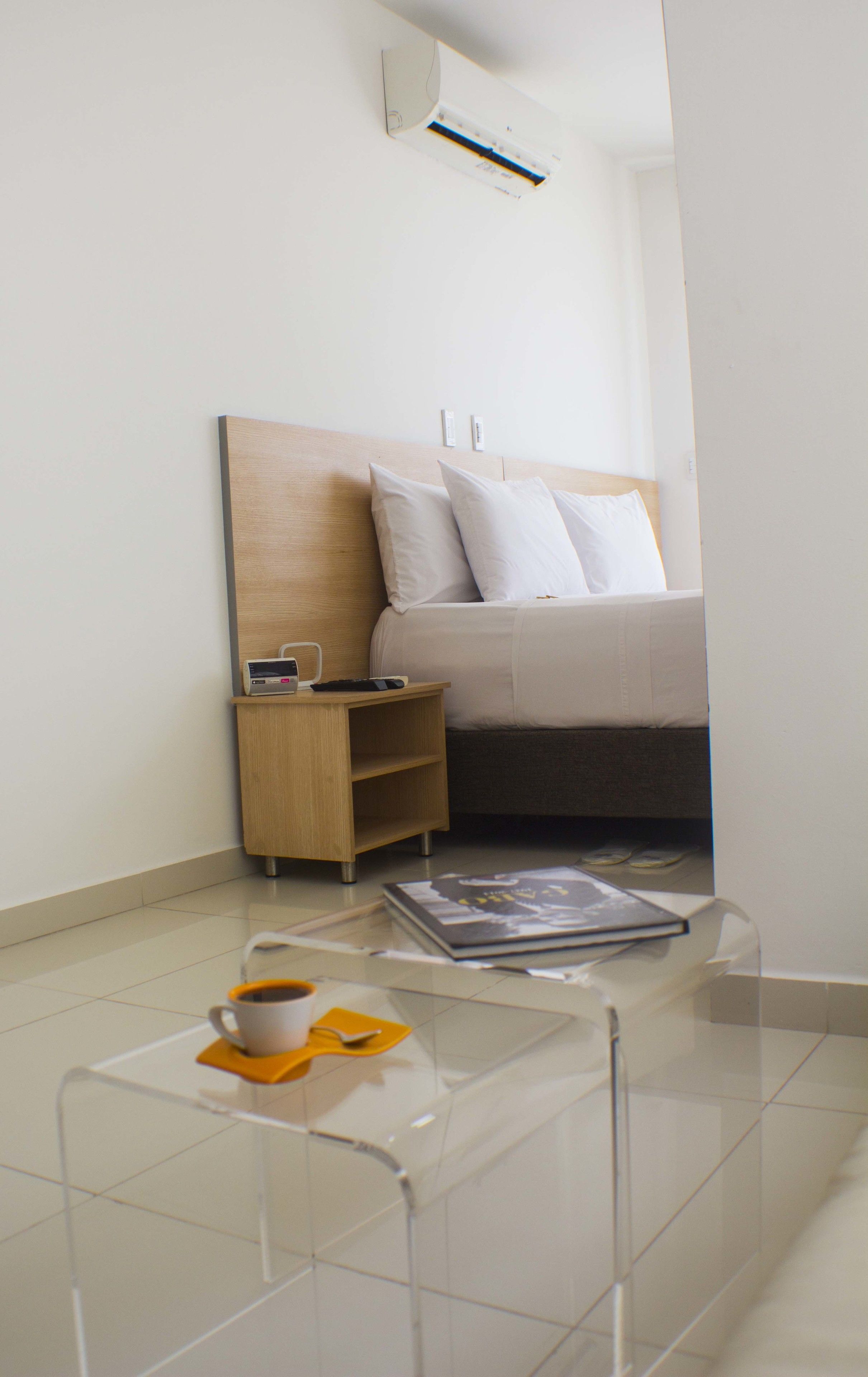 Una habitación de hotel con cama, mesita de noche y una pequeña mesa con una taza y un libro.