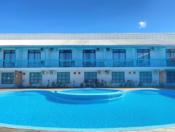 A two-story hotel with a swimming pool in front.
