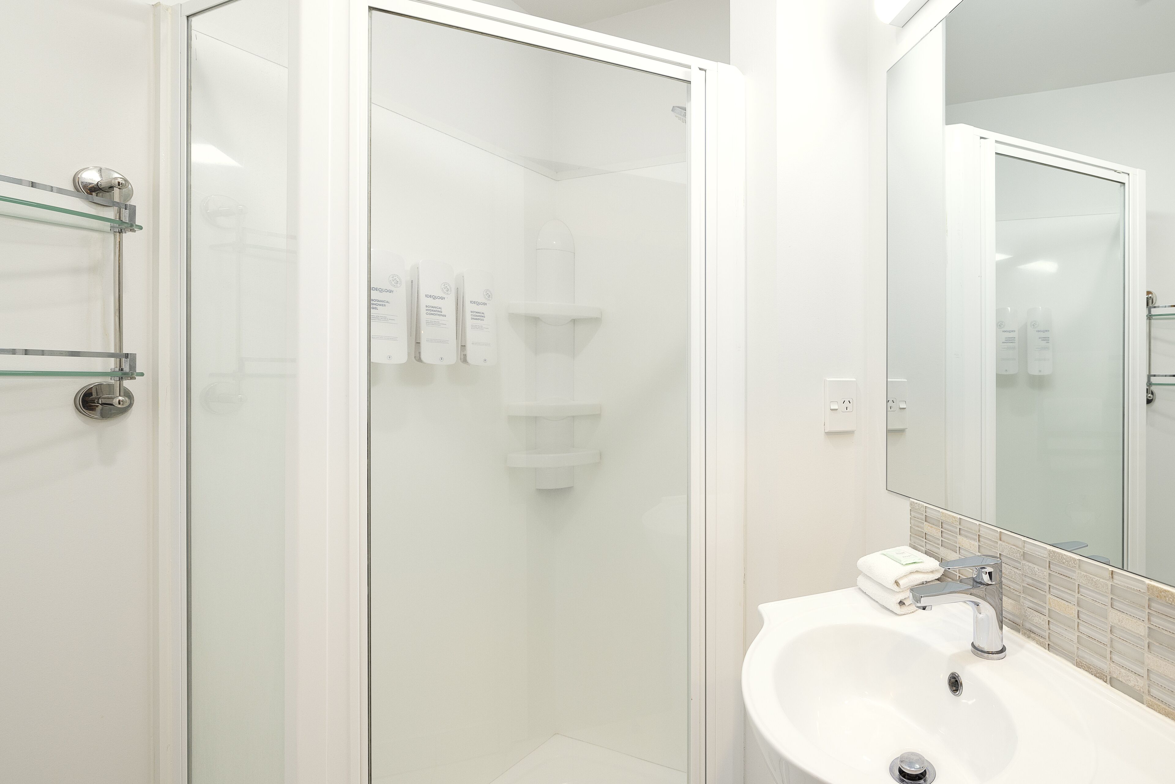 Un baño moderno con ducha de vidrio, un lavabo blanco y un espejo encima.