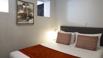 A neatly made bed with a brown blanket, white pillows, and a framed abstract painting on the wall.