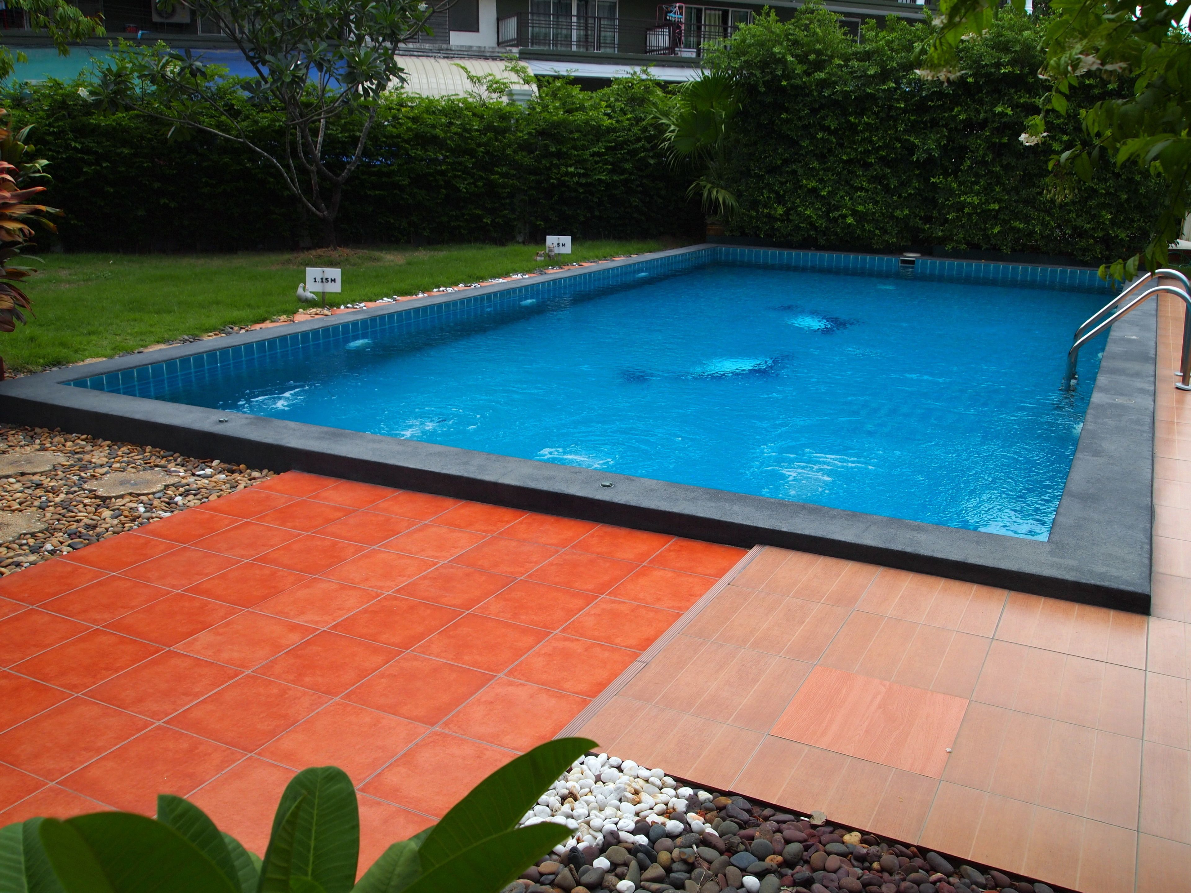 A rectangular swimming pool with a tiled edge, surrounded by a tiled deck area.