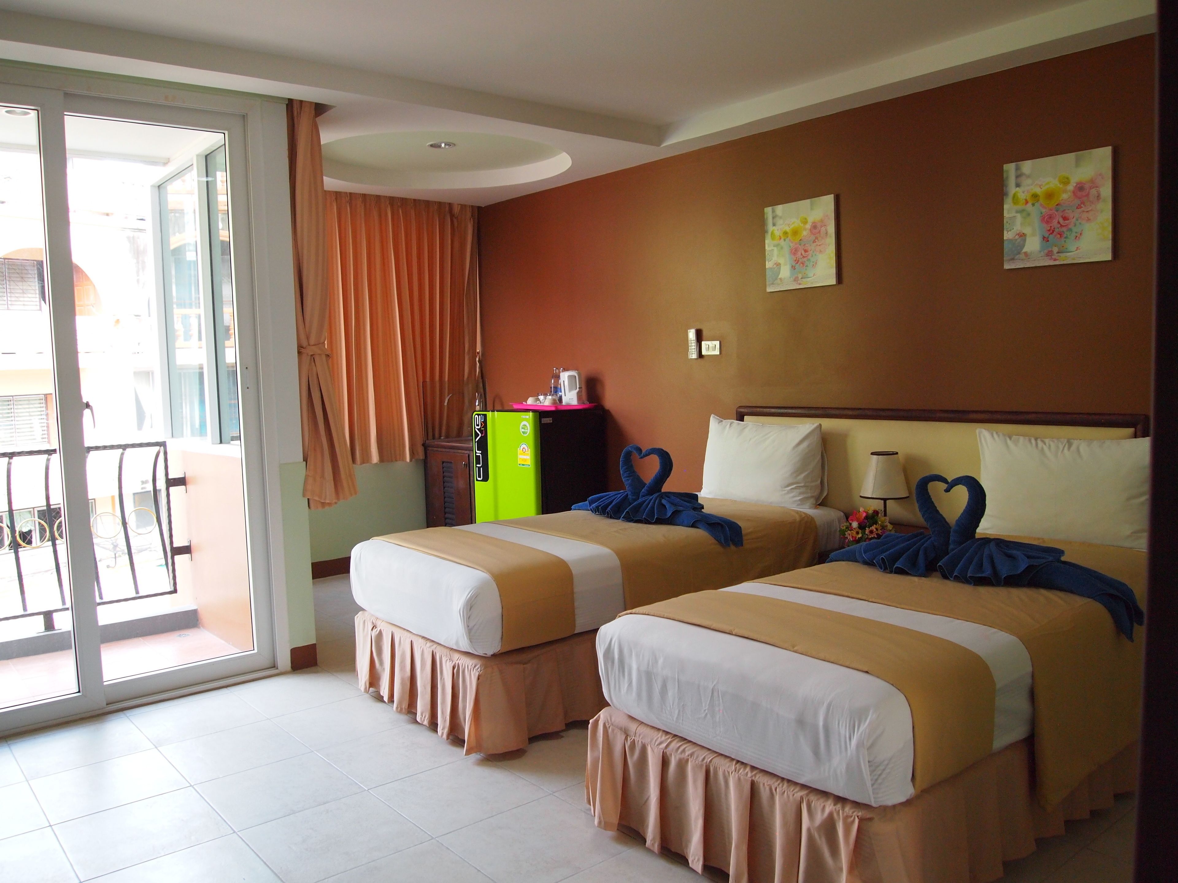 Quarto de hotel com duas camas, porta de correr para varanda, minibar e um quadro na parede.