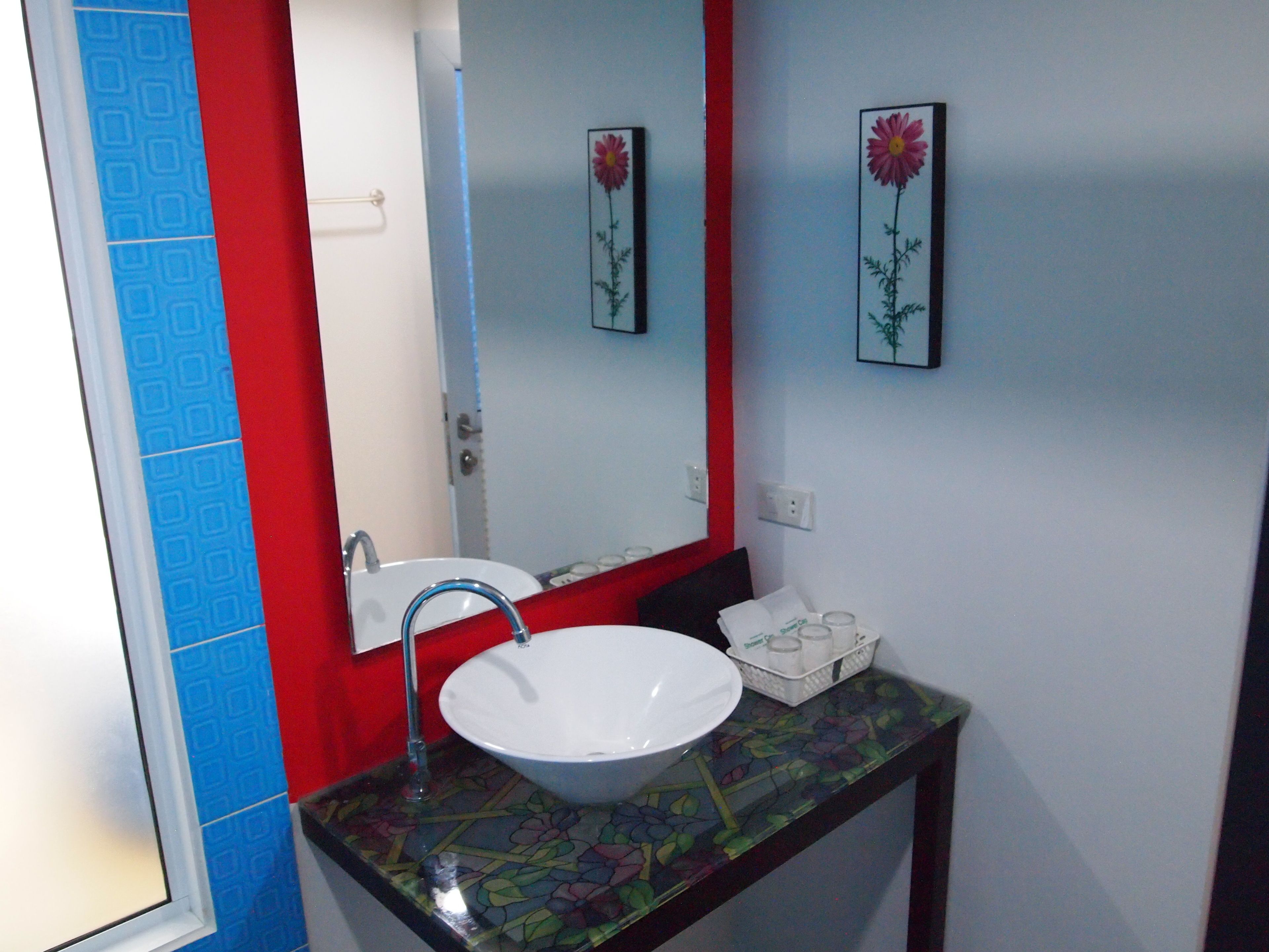 A bathroom with a white sink, red and blue patterned walls, and a mirror with floral artwork.