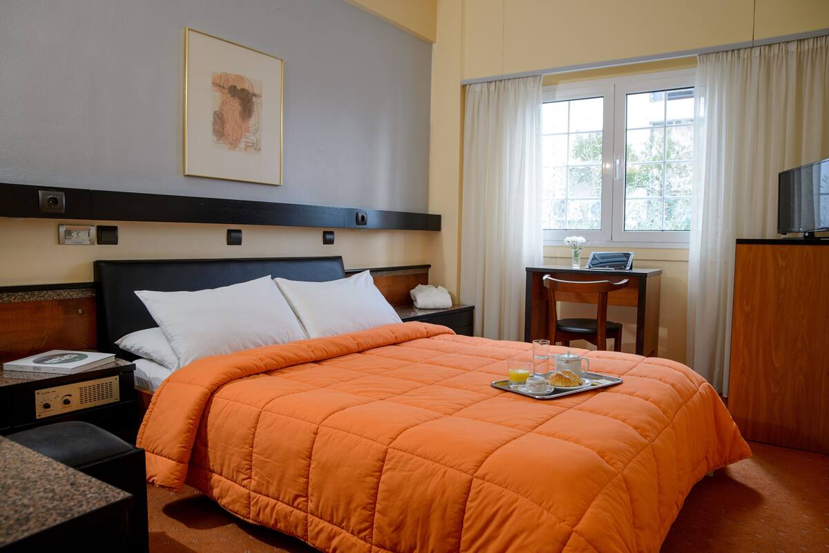 Ein Hotelzimmer mit Bett, Schreibtisch, Stuhl, Fernseher und einem fensterbepflanzten Fenster.