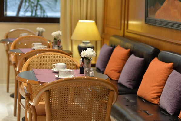 A dining area with wicker chairs, a table with a purple placemat, white flowers, and a sofa with orange and purple cushions. - Victory Inn (Athens)