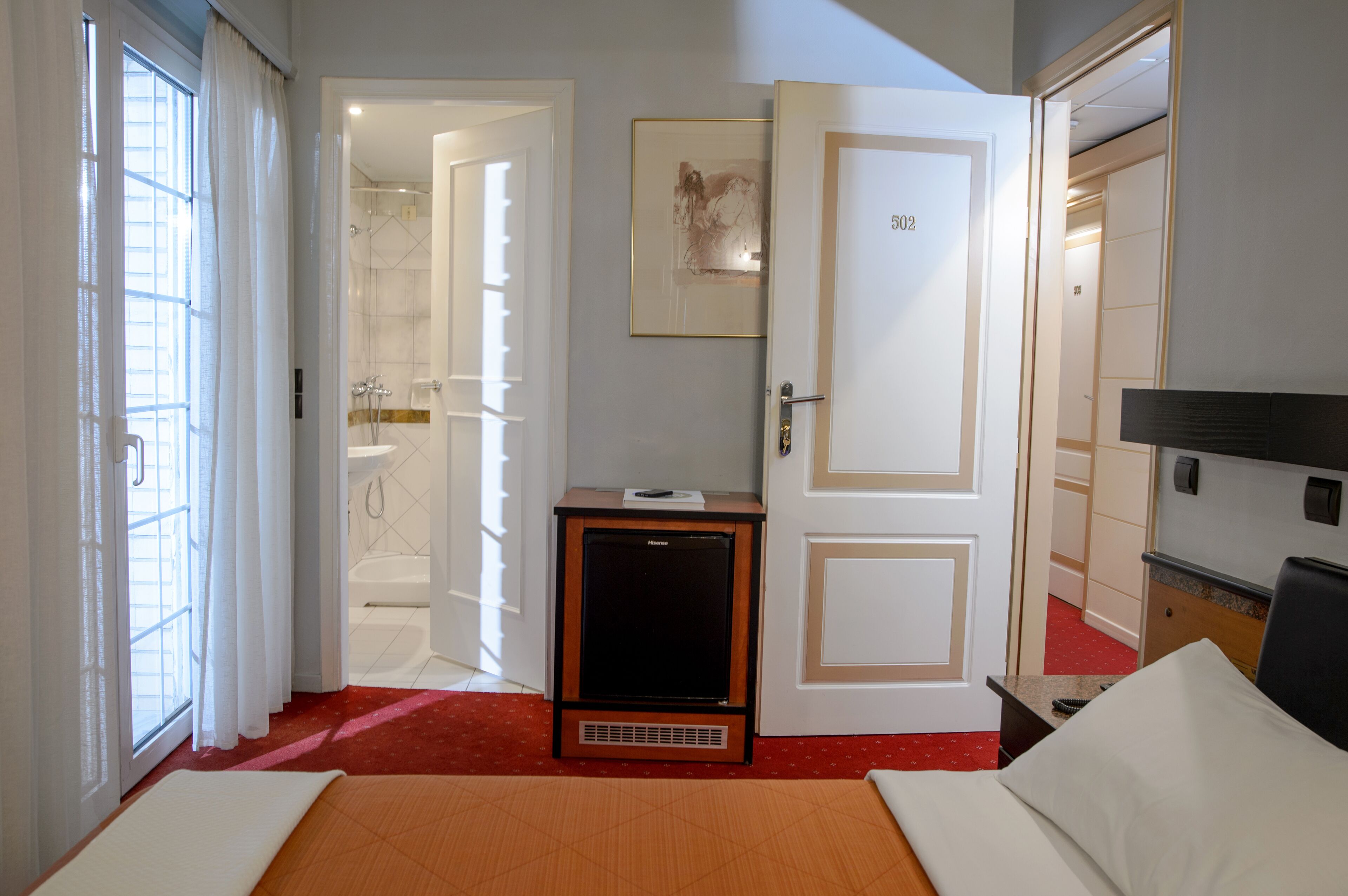 A hotel room with a bed, a small TV, a bathroom with a shower and bathtub, and a door with the number 502.