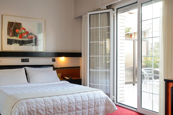 Una habitación de hotel con una cama, un cuadro, una mesita de noche, una lámpara y un ventanal corredizo al exterior.